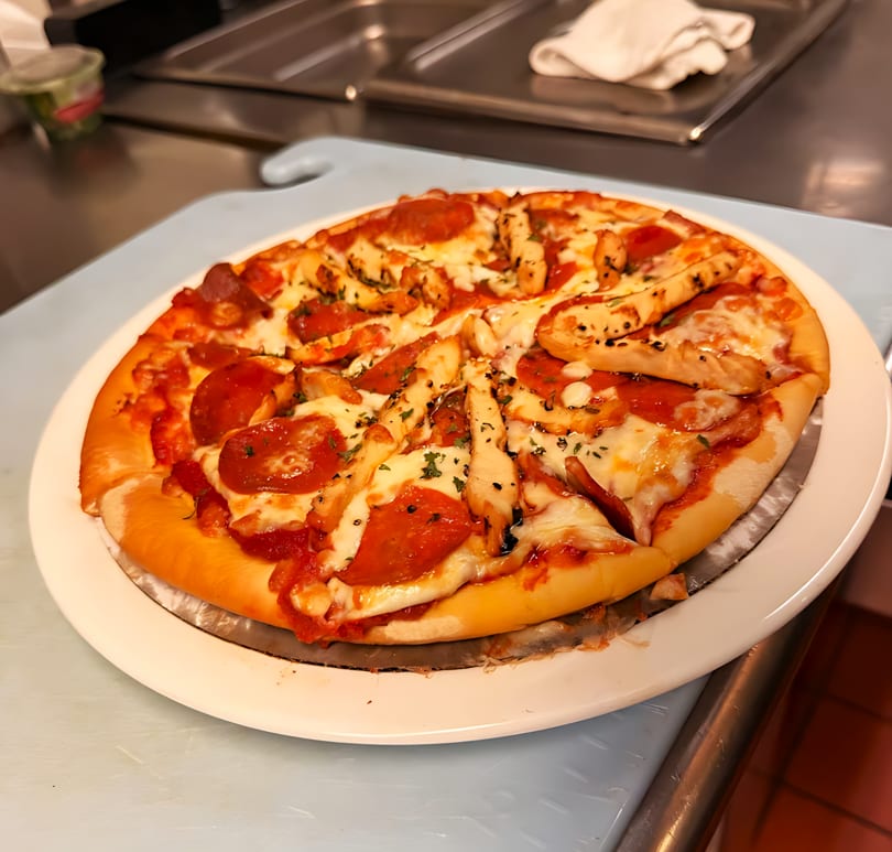 A freshly baked pizza with pepperoni and chicken, garnished with herbs, on a white plate.